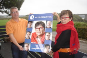 Med Alssundbroen i baggrunden præsenterer byrådskandidaterne Johnny Søndergaard og Karen Damm Alssundlistens team-inspirerede plakat.